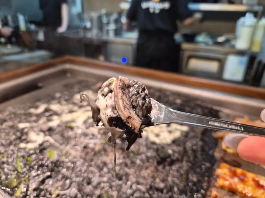 A bite of squid ink monjayaki topped with cheese