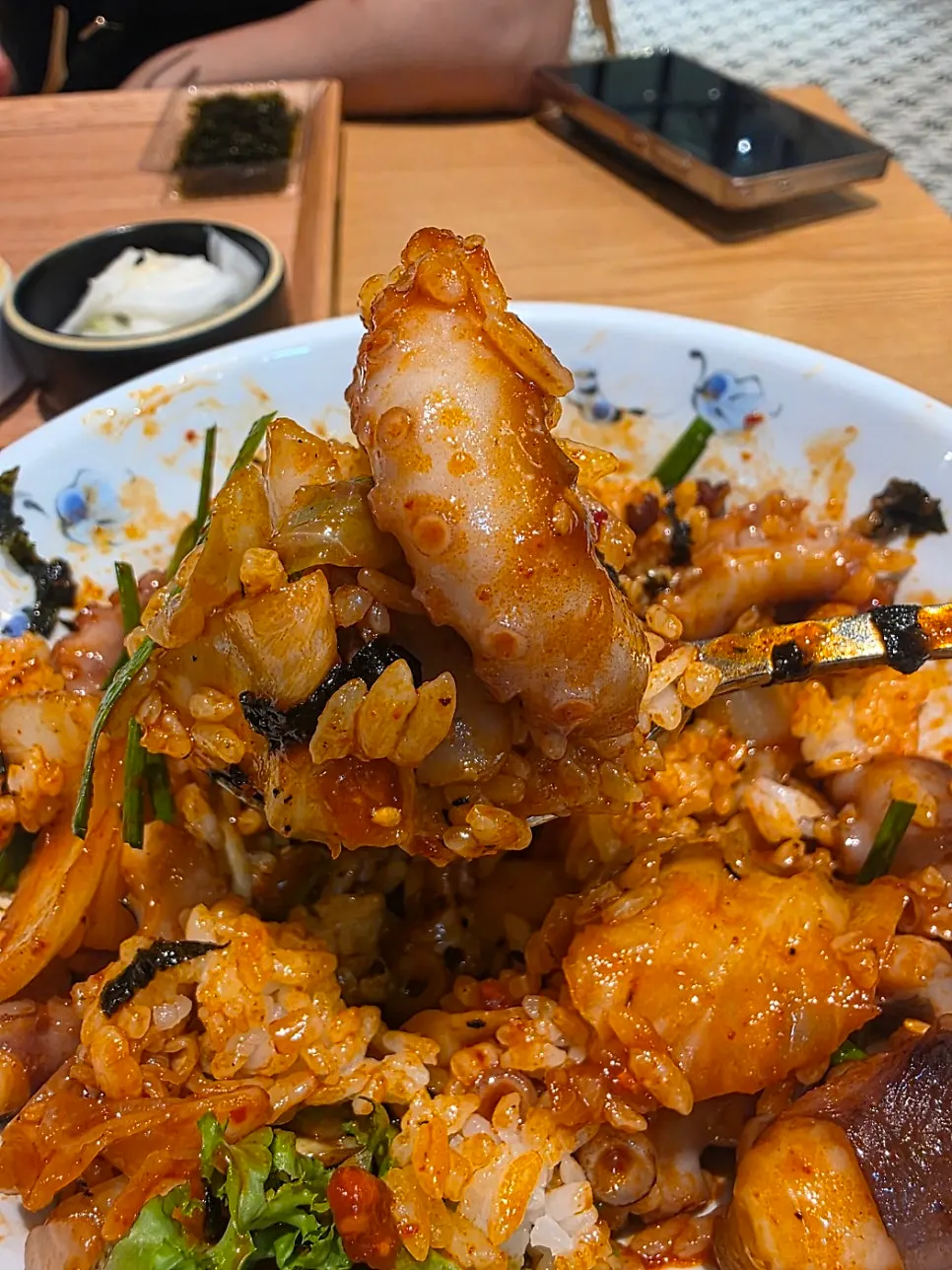 A piece of octopus stir-fry lifted up with chopsticks