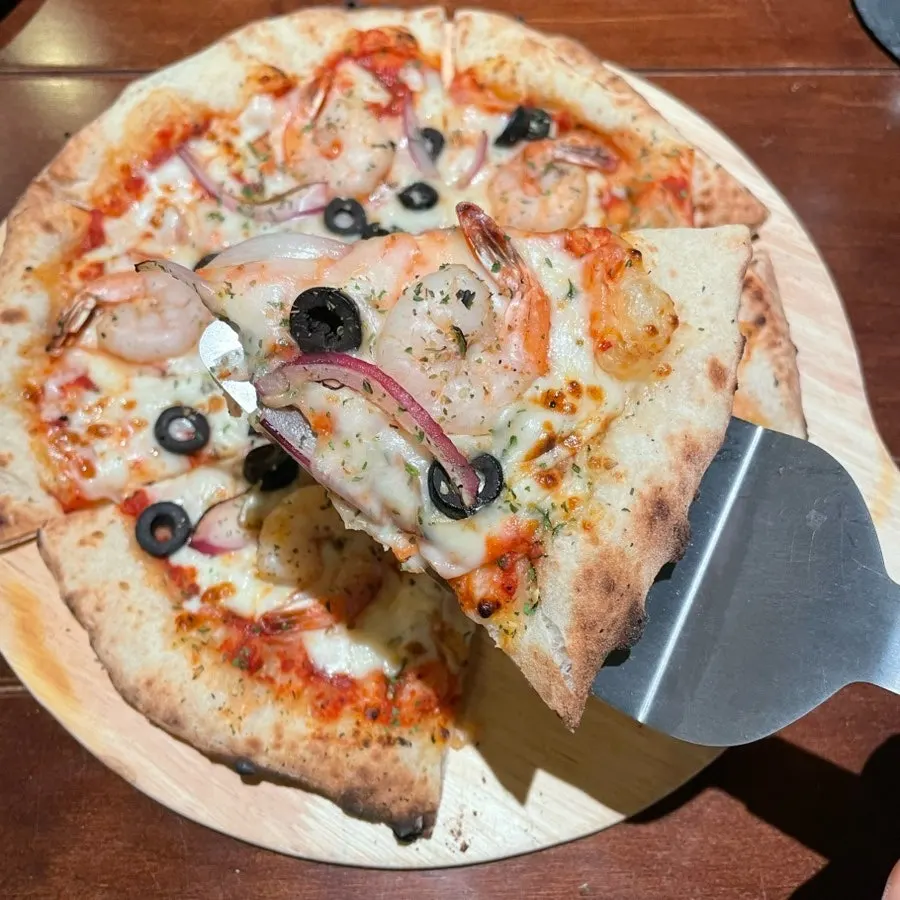 Slice of seafood pizza topped with shrimp and black olives