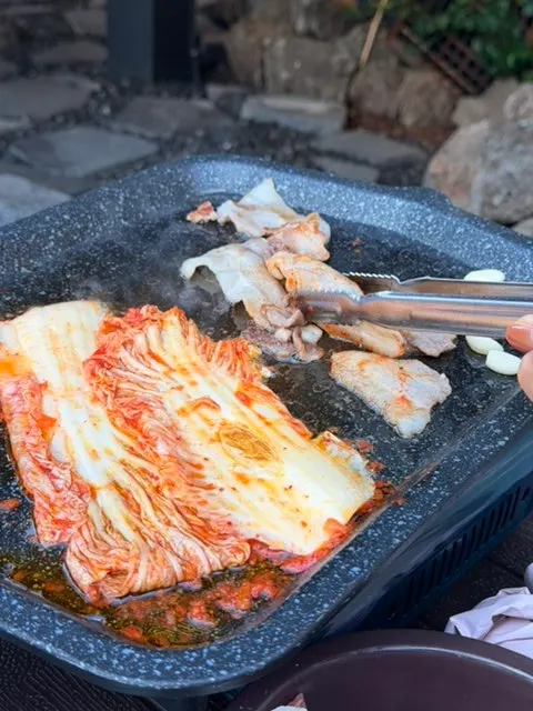 구운 김치에 올린 삼겹살 한 점과 마늘