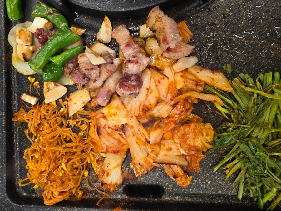 Well-grilled pork belly cooking alongside potato and shishito peppers