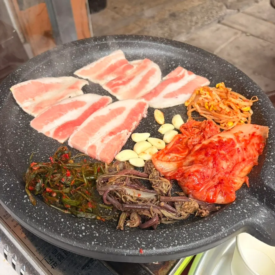불판에 올린 삼겹살과 마늘, 파김치, 콩나물