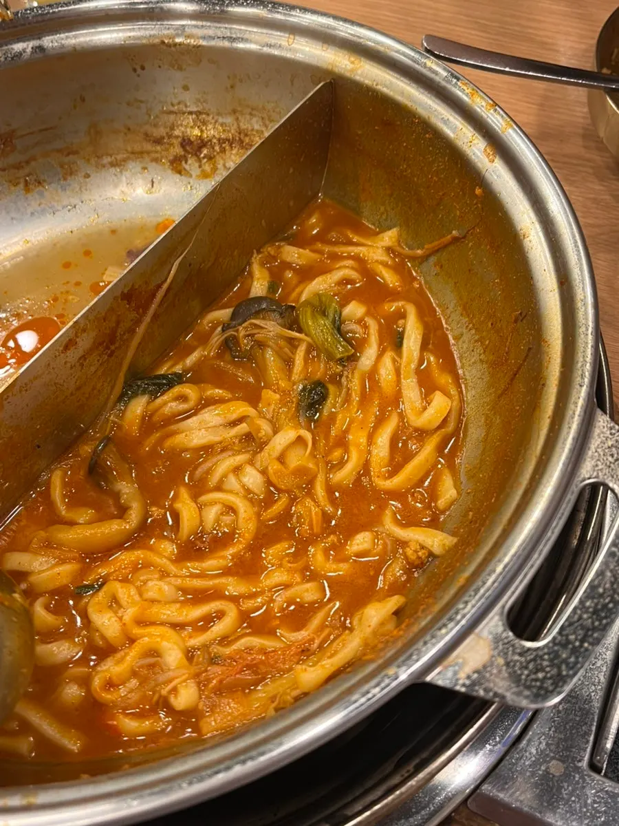Pot of half-and-half broth simmering with mandu and meat