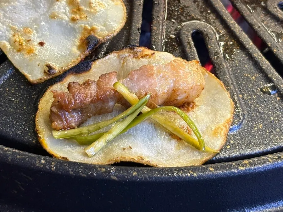A piece of pork belly topped with grilled potato and minari
