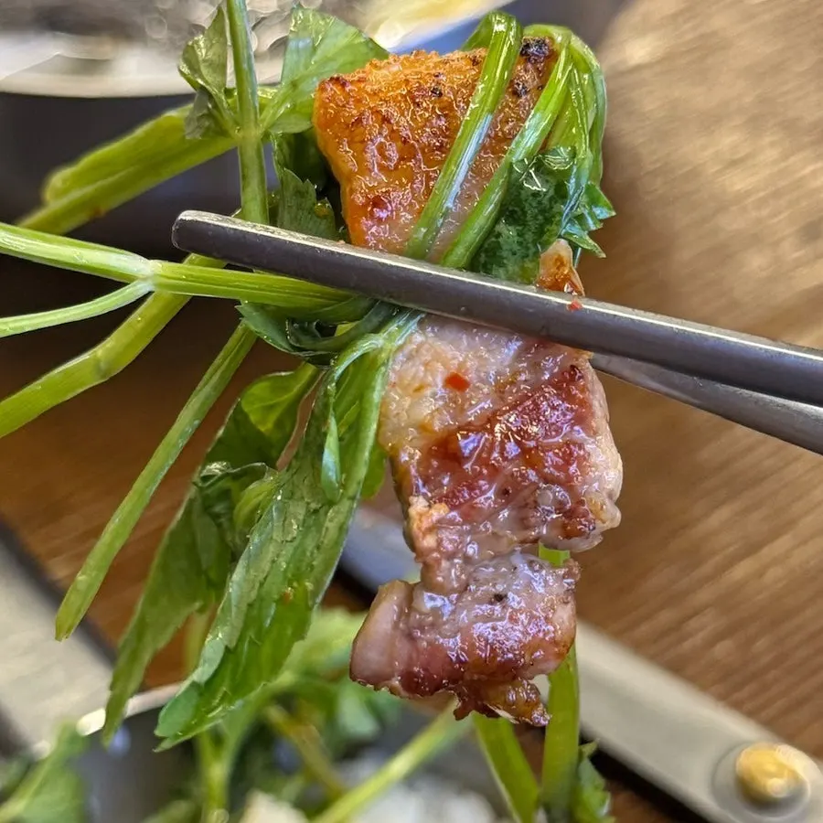 Mesa con el samgyeopsal ya asado junto a minari, brotes de soja y kimchi