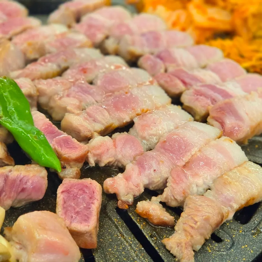 Pork belly grilling on a charcoal grill plate