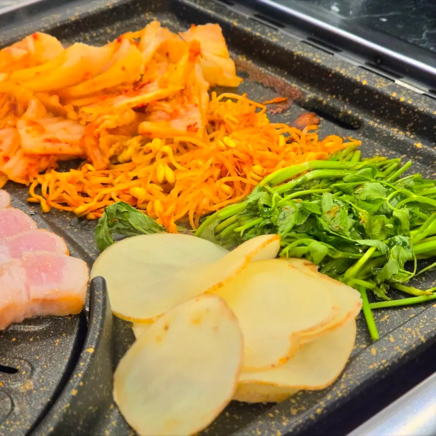 Minari, napa cabbage kimchi, and potato cooking on one side of the grill