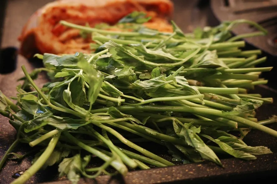 Kimchi, bean sprouts, and minari grilling alongside the pork belly