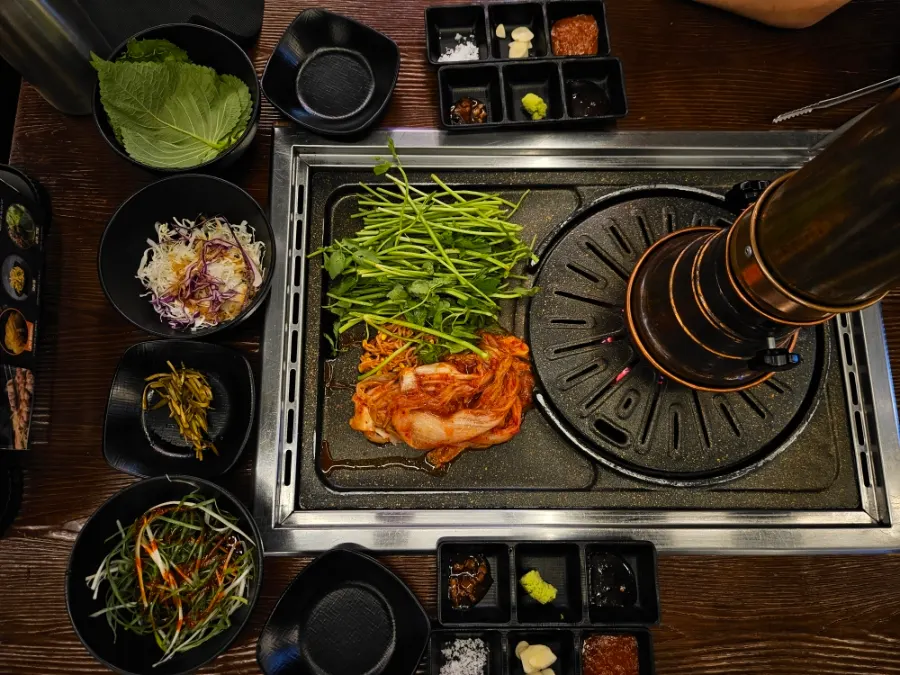 Pre-set side dishes and minari and kimchi on the grill