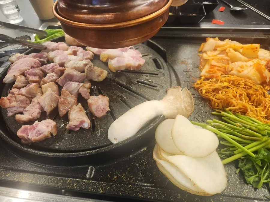 불판 위 삼겹살과 콩나물, 김치, 미나리 사이드
