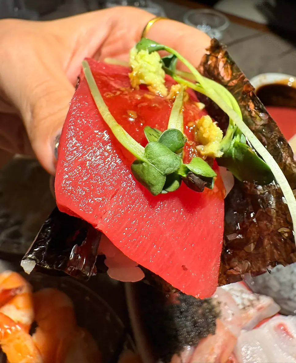A shot glass of soju alongside sashimi and shrimp