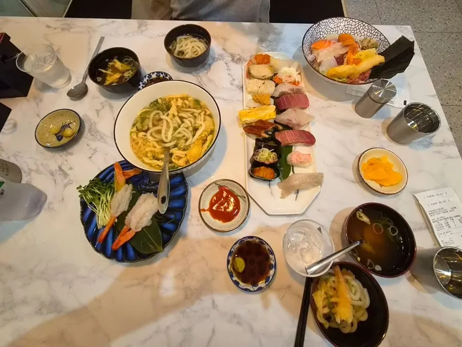 Full spread of sushi, sashimi, kaisendon and udon on the table