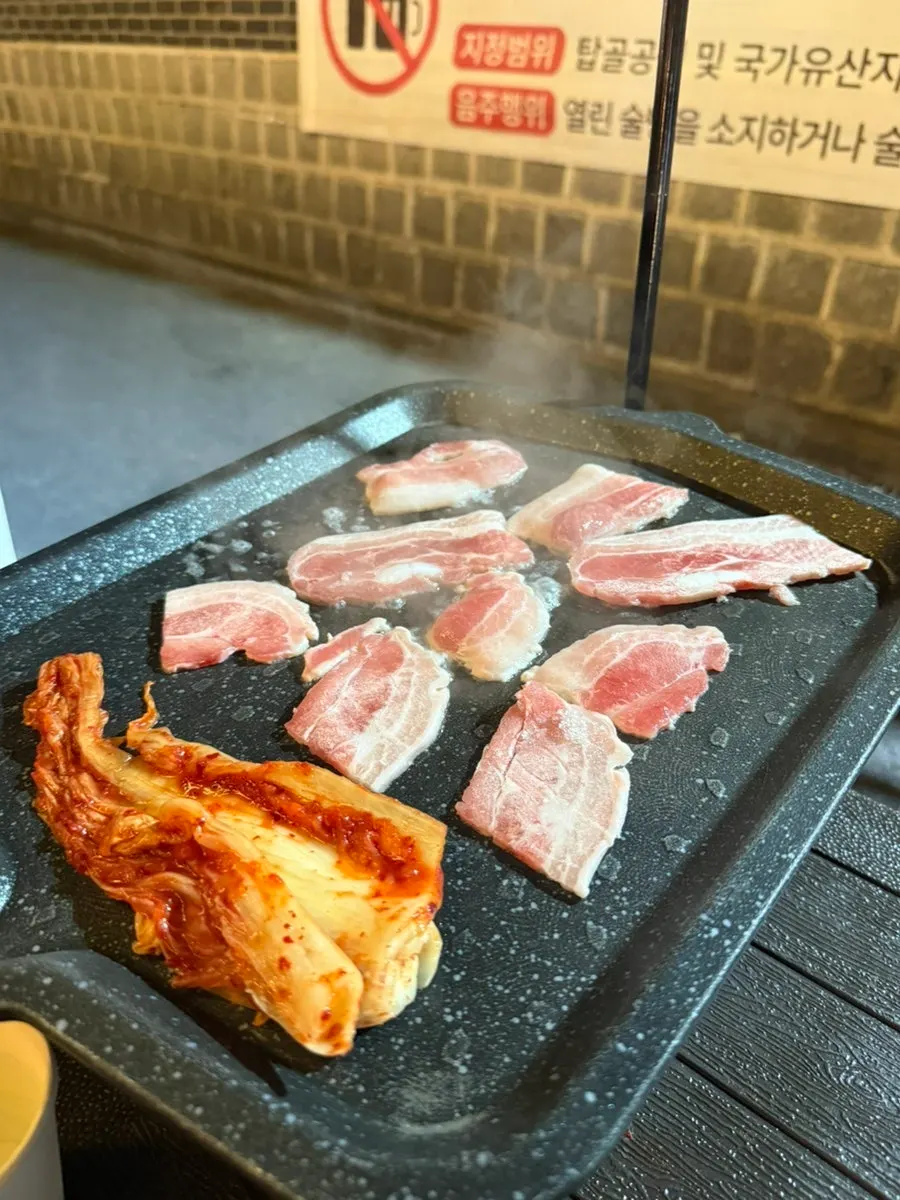 불판에 올린 냉동삼겹살과 밑반찬