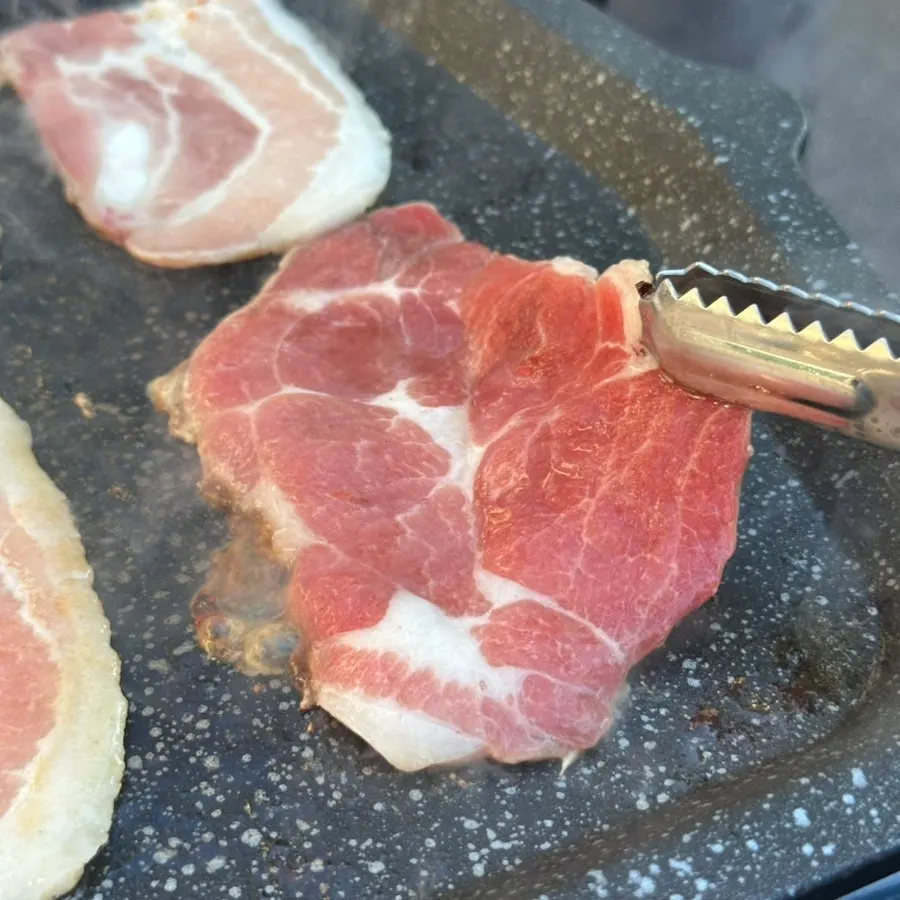 Thin-cut pork belly turning golden on the grill