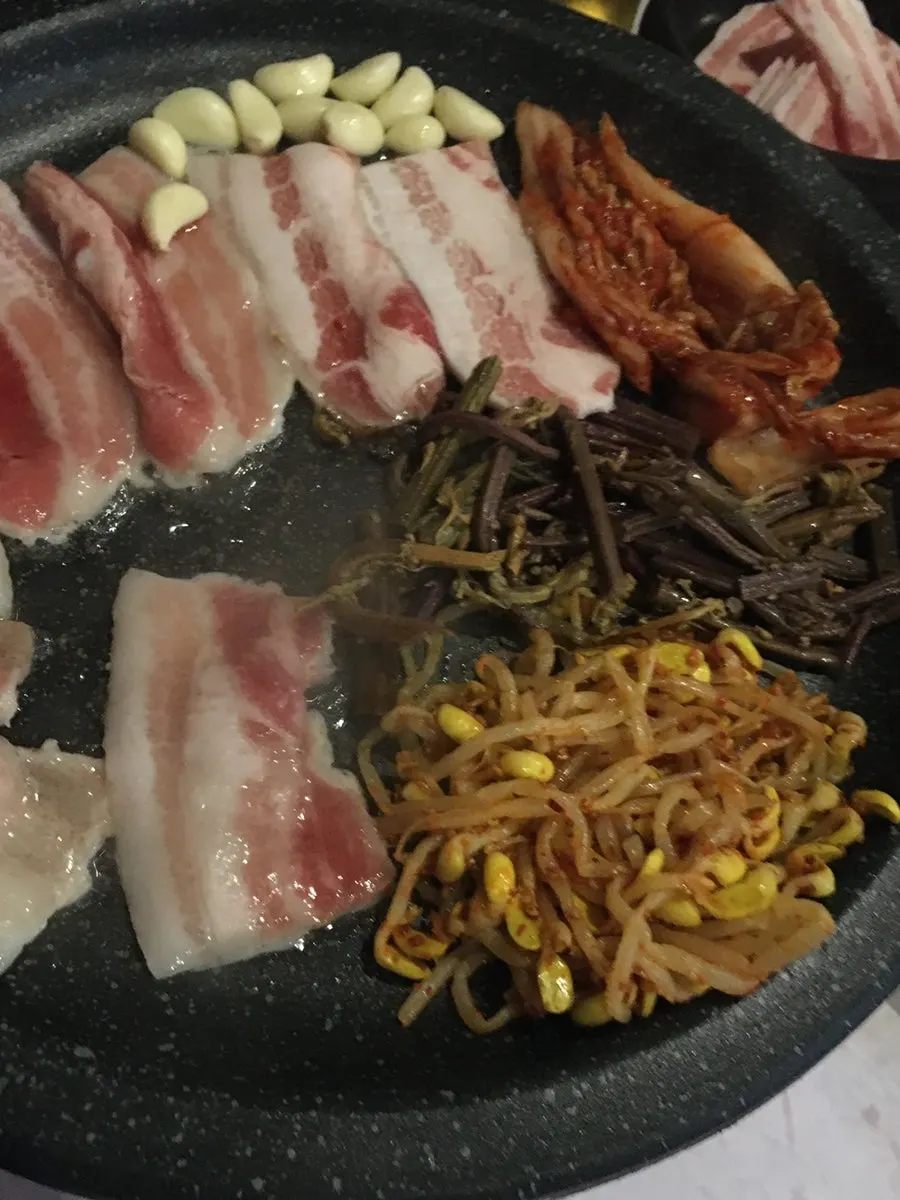A grill loaded with kimchi, bean sprouts, bracken fern, and garlic together