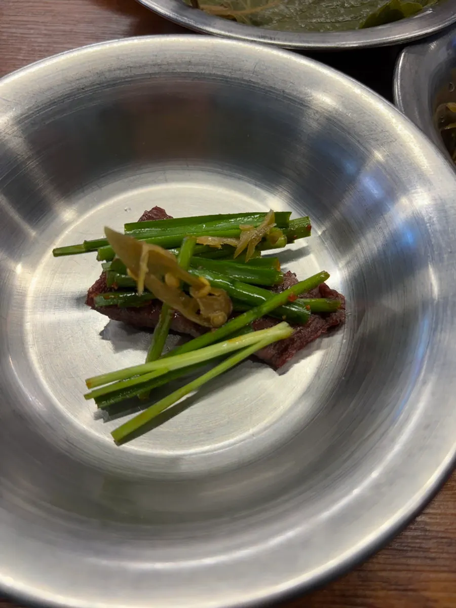 A piece of beef topped with chive salad and pickled chili