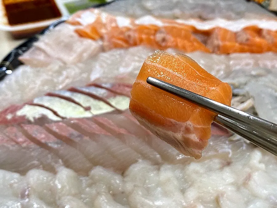 A piece of salmon sashimi held with chopsticks