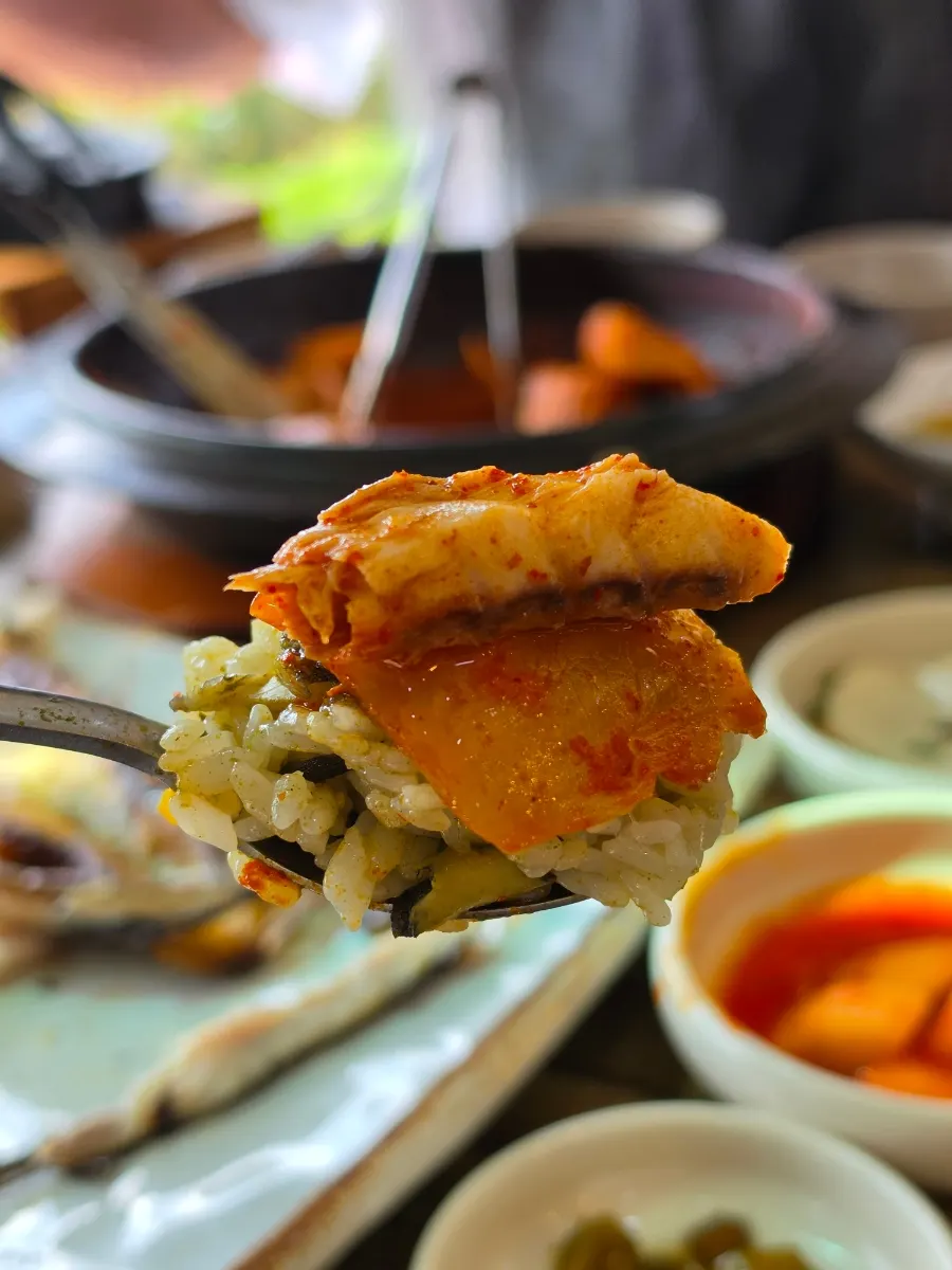 A wrap of ssam greens with rice, mackerel and old kimchi