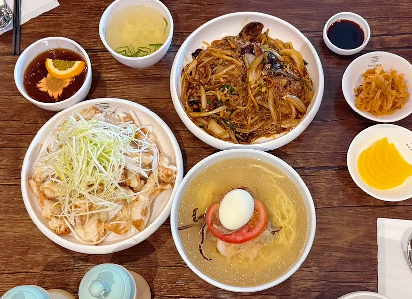 Table spread with jungwa naengmyeon, japchaebap, and sweet and sour pork