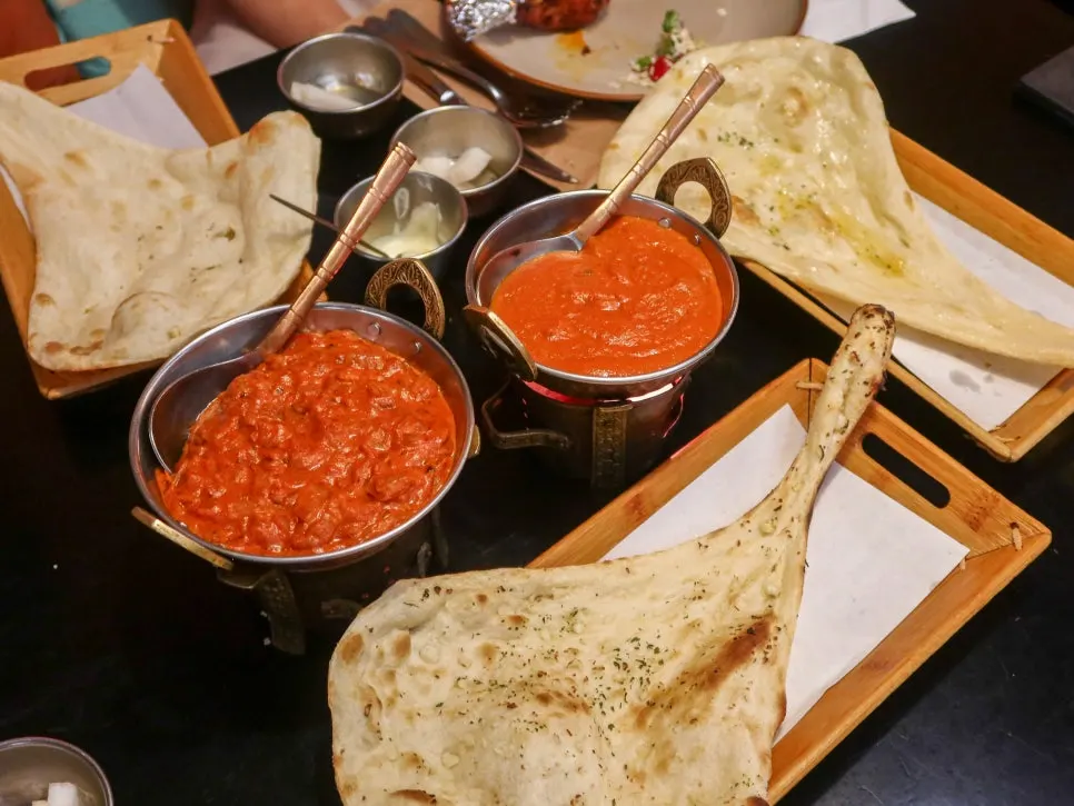 Table spread of tikka masala, korma curry, and three kinds of naan