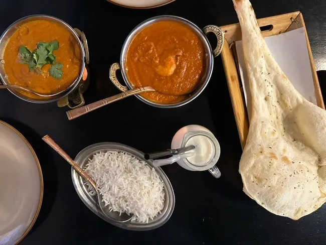 Table spread with butter chicken curry, prawn makhani, naan, and mango lassi
