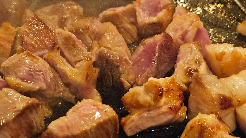 Grill pan with mushrooms and potatoes cooking alongside the meat