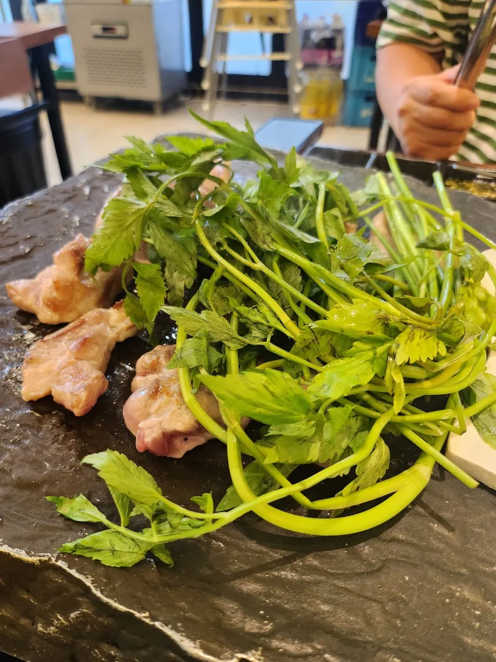 Minari and golden-browning samgyeopsal on the cast-iron grill