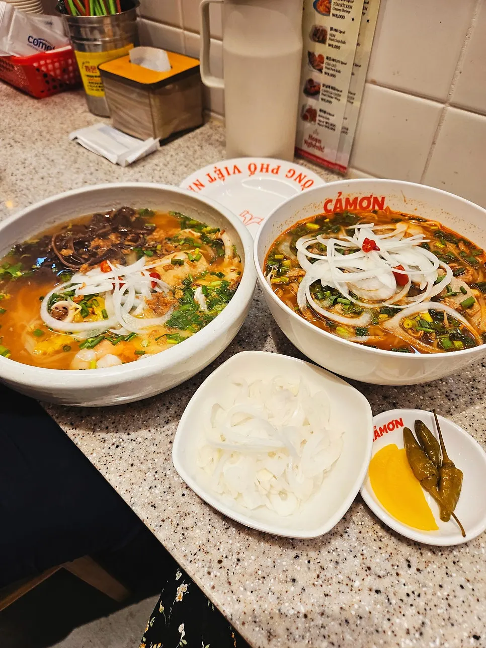 Two bowls of pho and a plate of stir-fried morning glory on the table