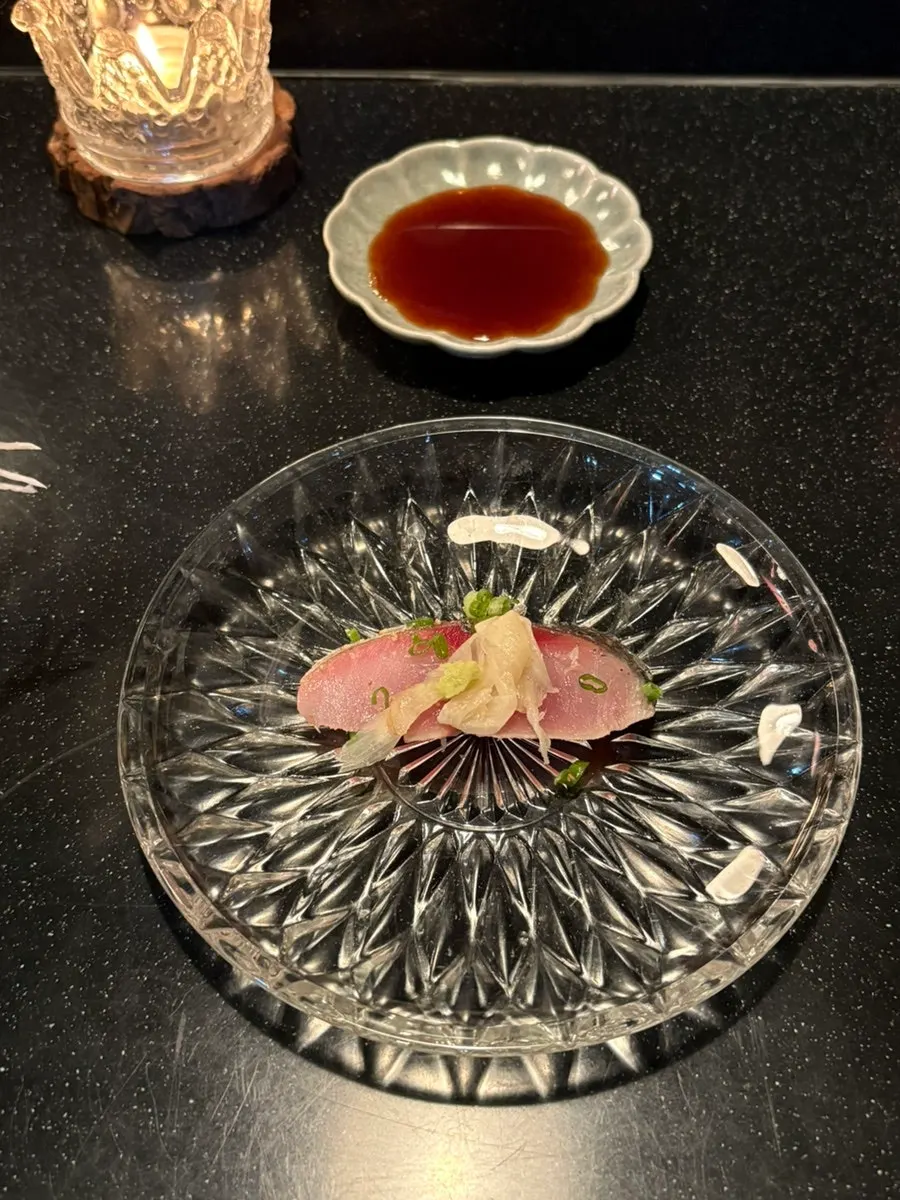 A slice of mackerel sashimi held with chopsticks