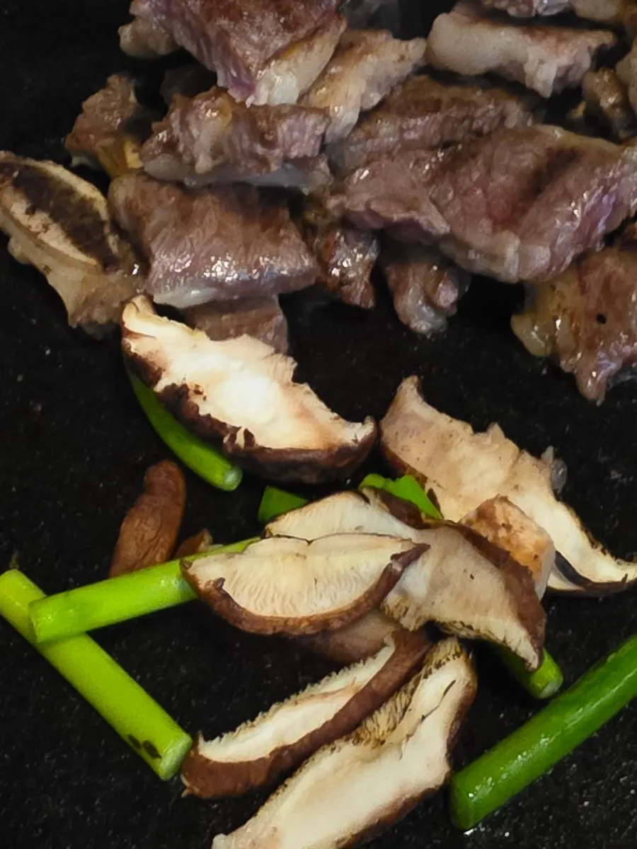 Shiitake mushroom and garlic scapes grilling alongside the meat