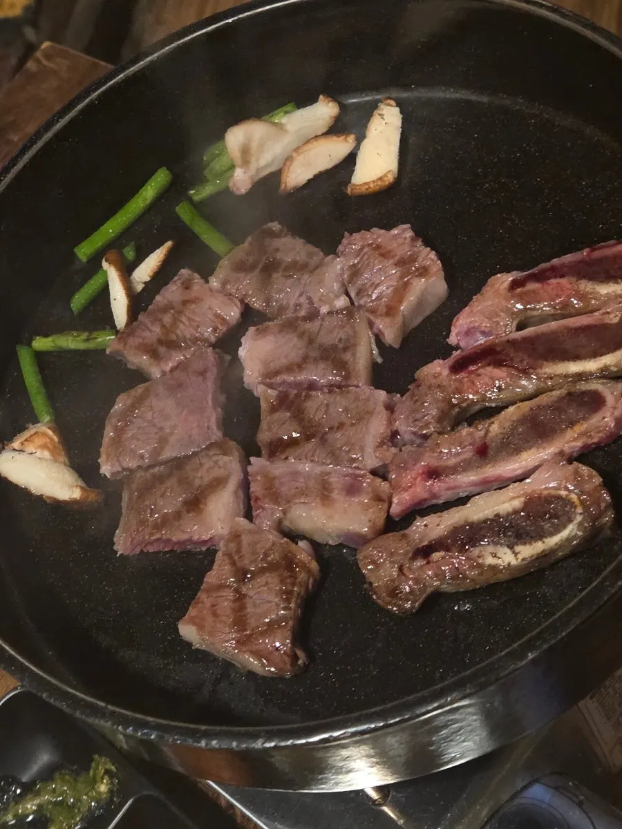 Grill pan with garlic scapes and mushrooms cooked alongside the meat