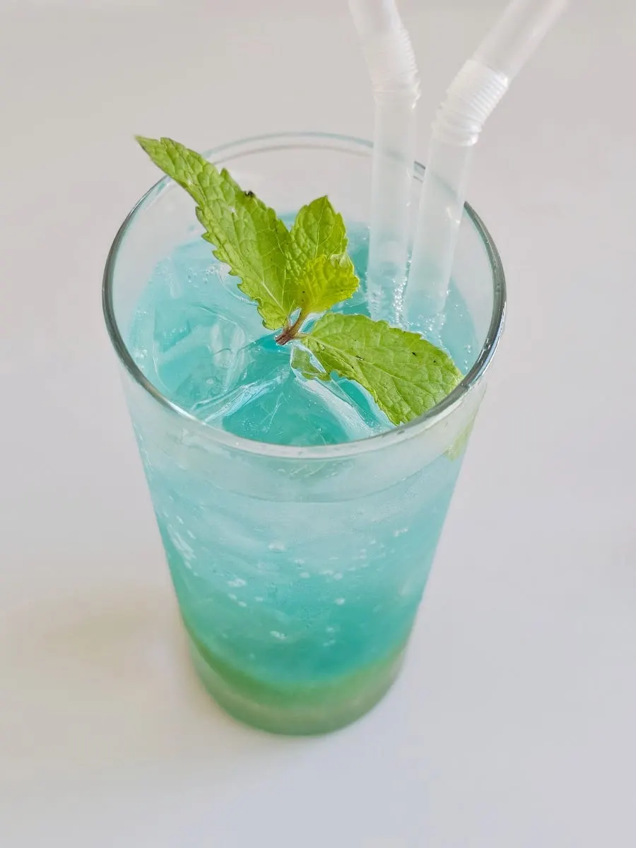 Glass of blue yuja ade with citron bits settled at the bottom