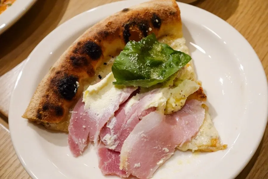 A lifted slice of cotto e ricotta pizza