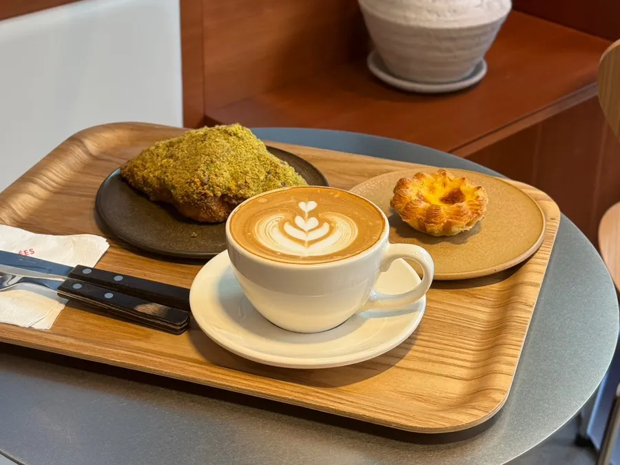 Café latte, pistachio croissant, and egg tart set on a table