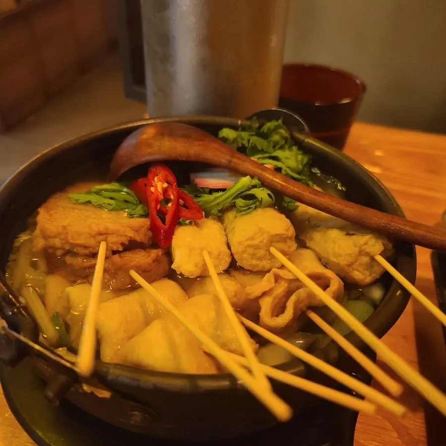 Oden hot pot broth topped with crown daisy and red chili