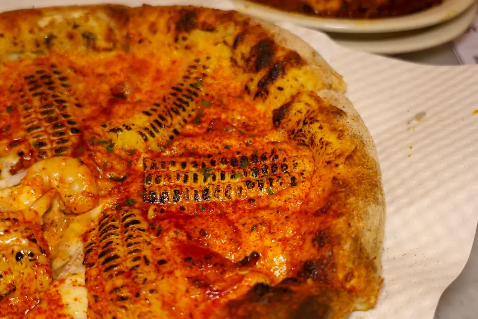 A slice of pizza with a strip of grilled corn pulled off
