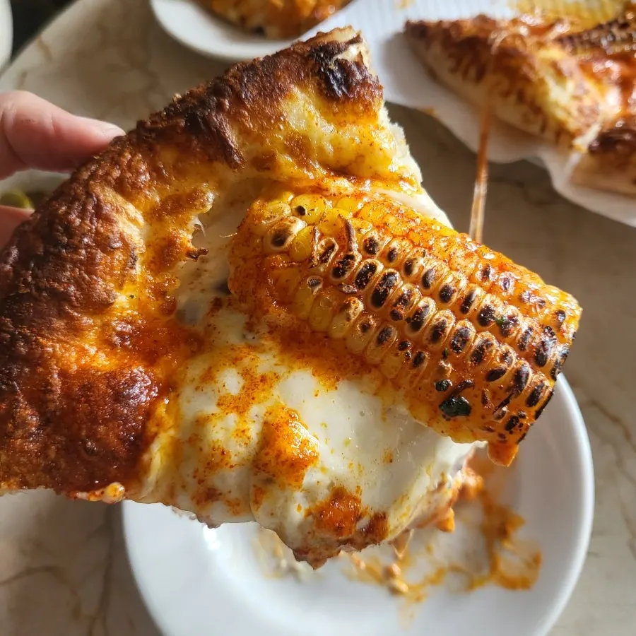 A slice of corn pizza lifted up showing the cross-section
