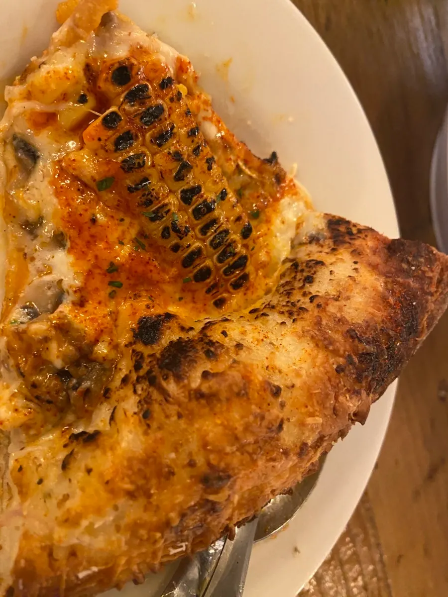A golden-brown slice of sweet corn pizza