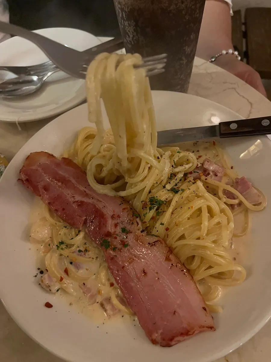 Alfredo cream pasta topped with a whole piece of bacon