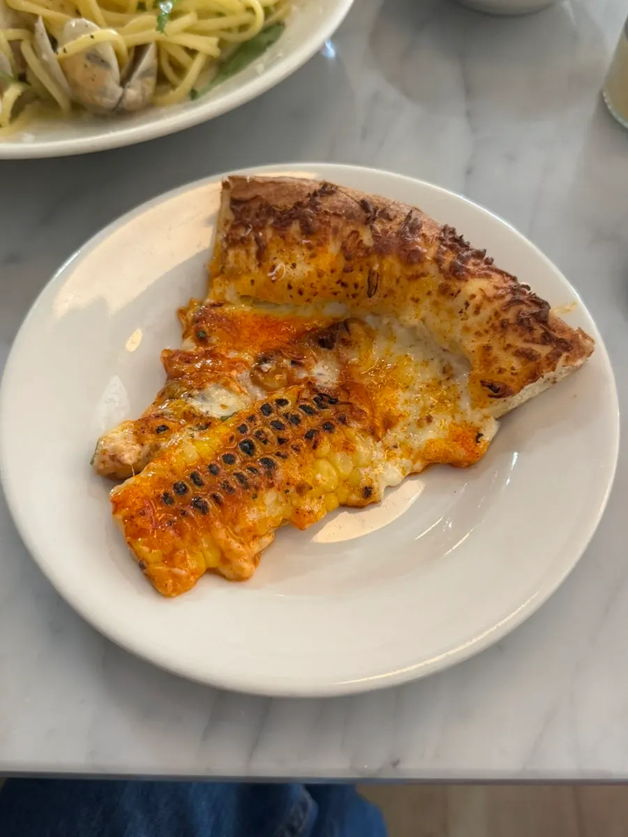 Slice of corn pizza topped with bacon and chili shrimp