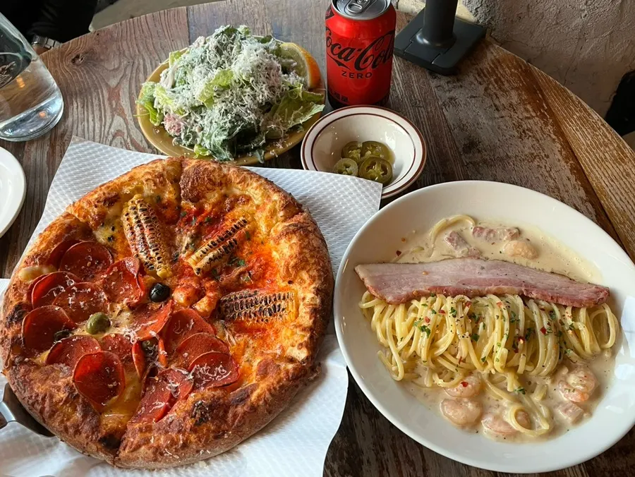 Table spread with salad, half-and-half pizza, and cream pasta