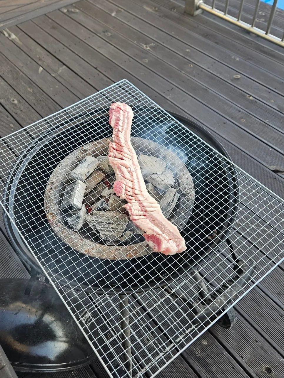 Pork belly grilling over charcoal at the outdoor barbecue area