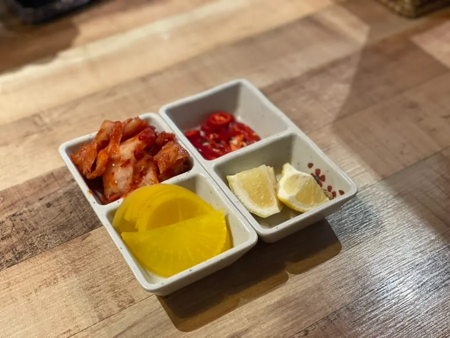 Side dish plate of kimchi, chili, pickled radish, and lemon