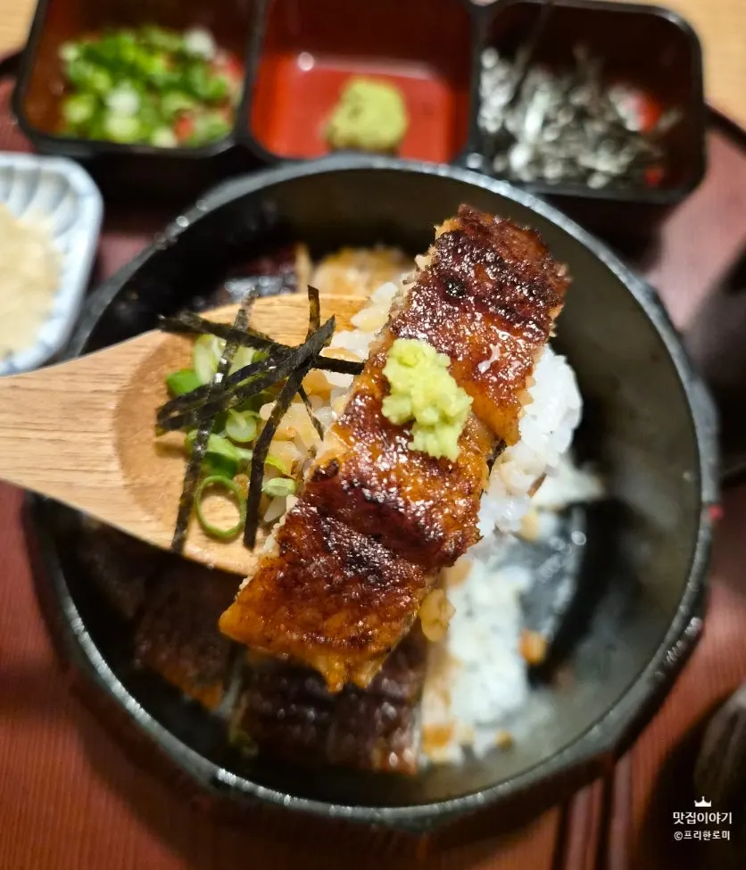 A bowl of eel rice topped with scallion, wasabi, and seaweed