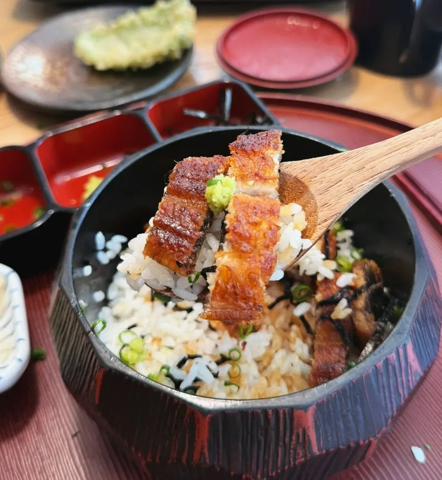 A spoonful of rice topped with two pieces of eel and wasabi