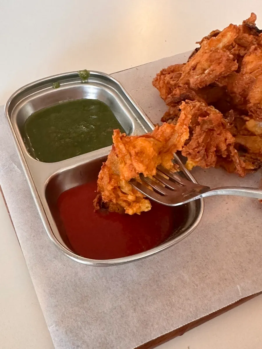 An onion fritter dipped in sauce