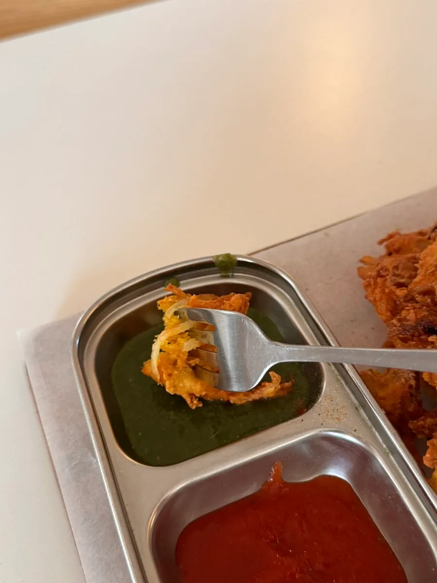 Onion fritter being dipped in green sauce