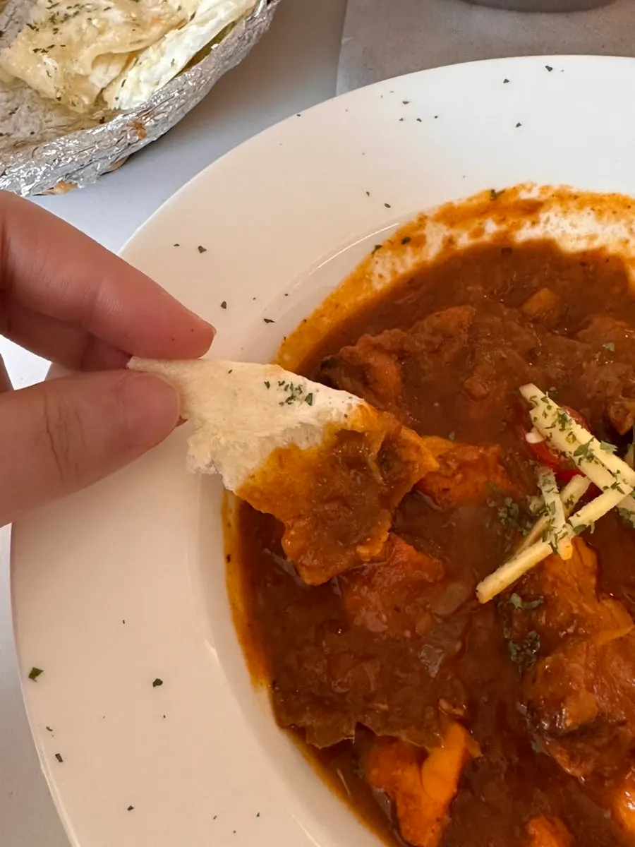A piece of garlic naan dipped into the curry