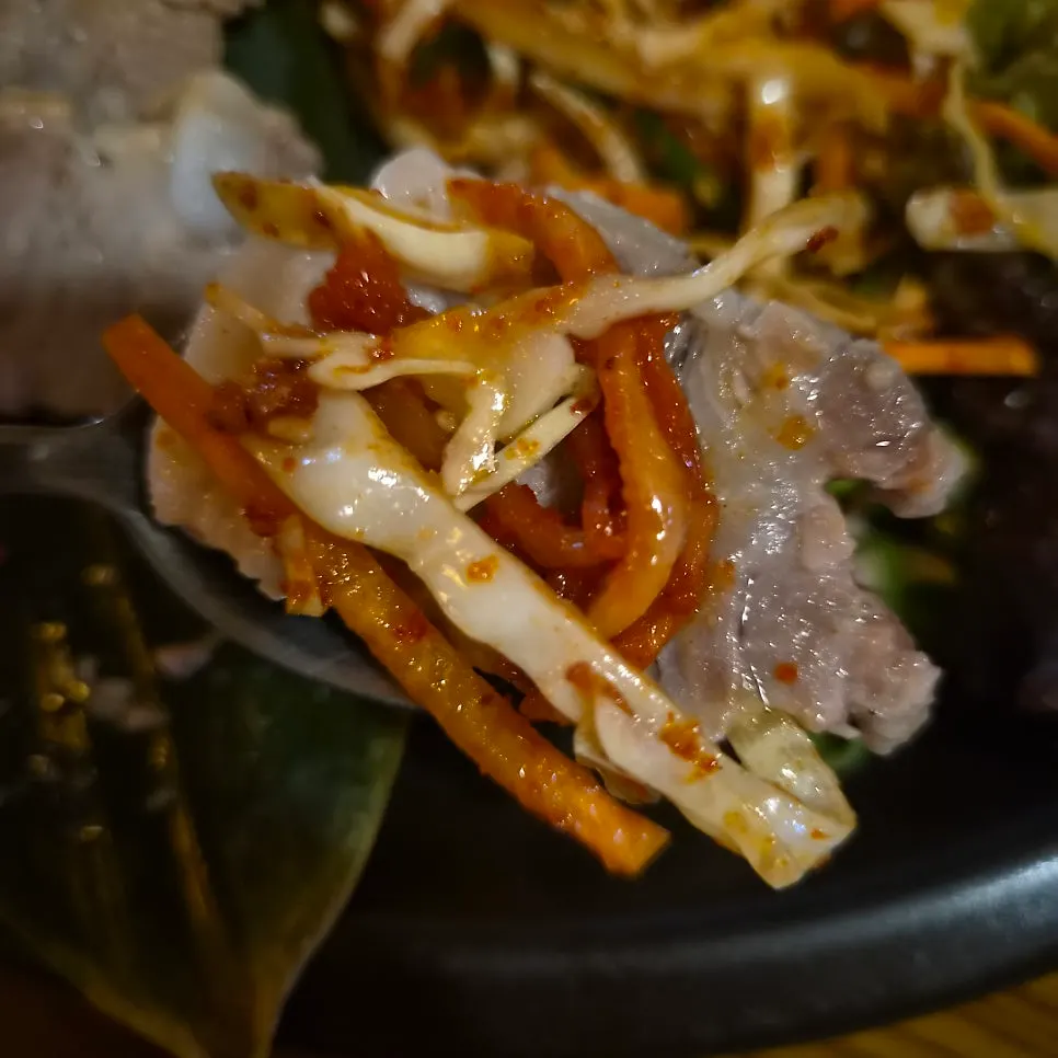 A piece of bossam paired with cabbage kimchi and radish kimchi