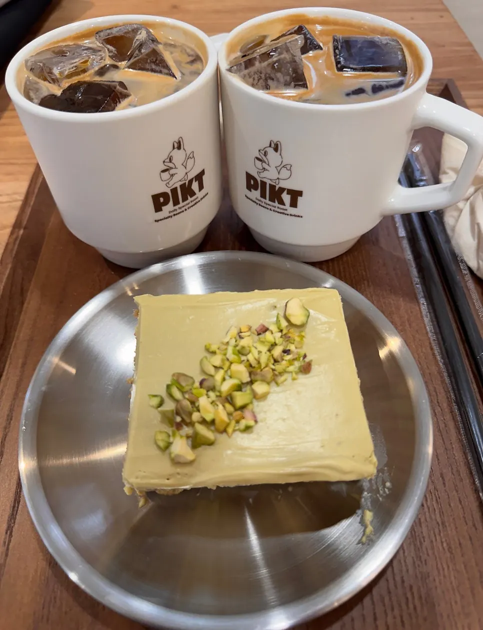 Two iced americanos and pistachio tiramisu served on a tray